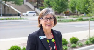 Jill smiling with a black blazer and statement necklace
