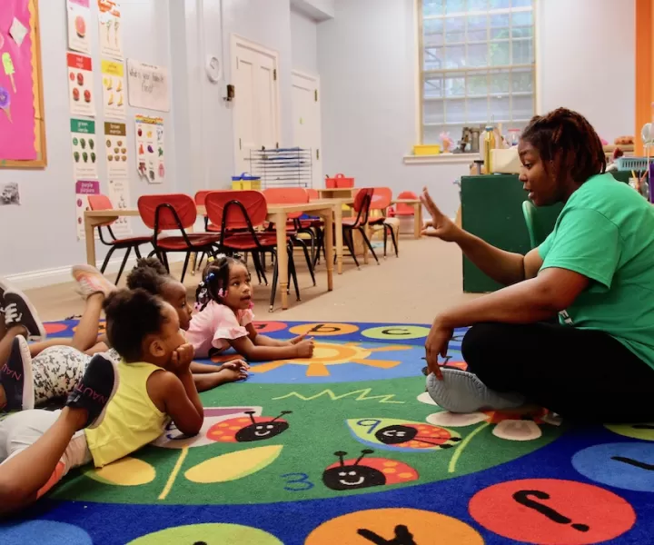 girls on carpet area while teacher teaches