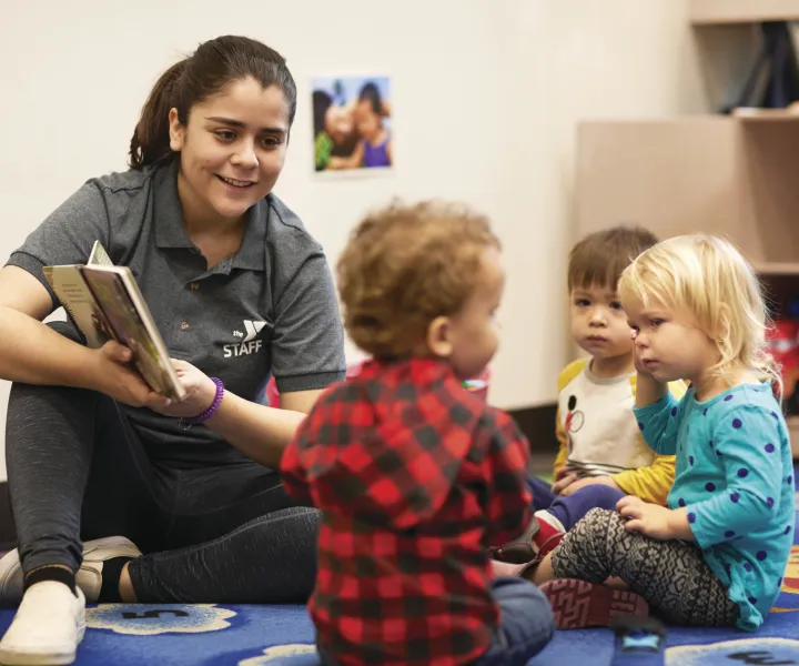 Woman in Y shirt reading a book to three toddlers.